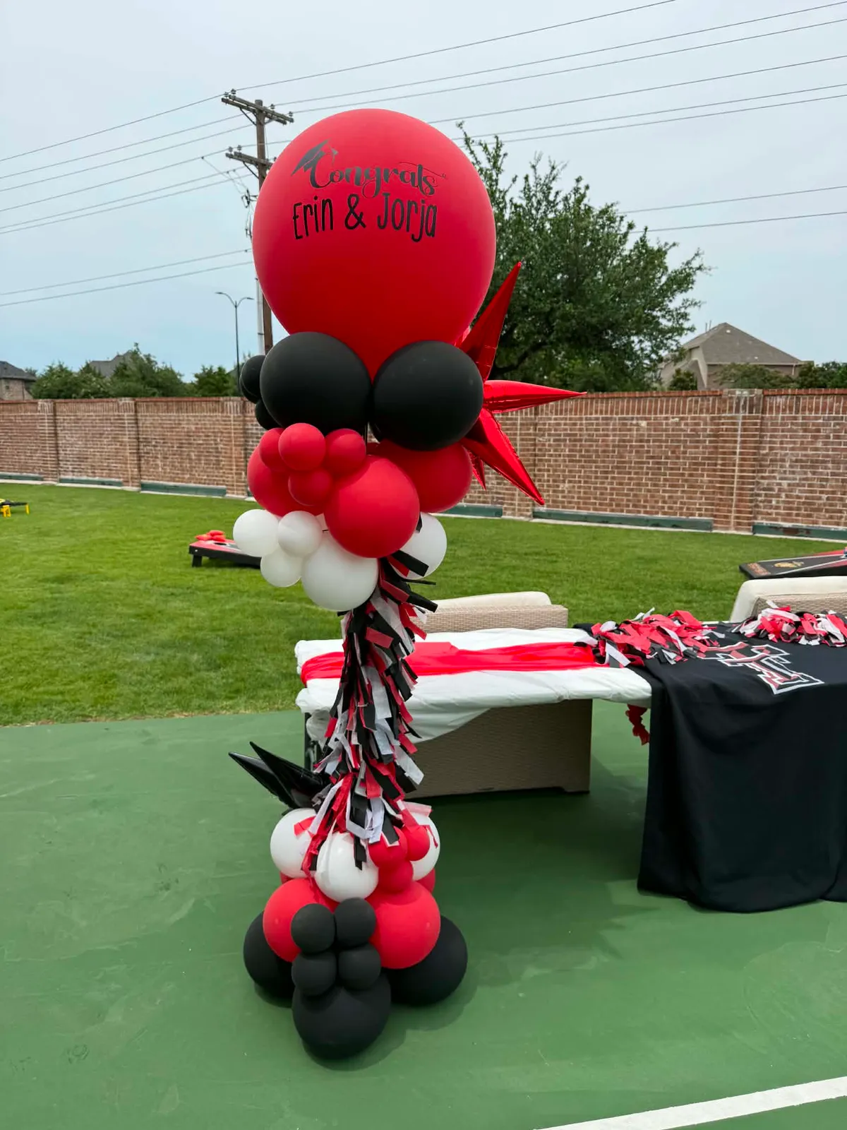 Outdoor red, black, and white balloon column with a Congrats Erin and Jorja graduation topper, a red foil star, and a red, black, and white tassel garland