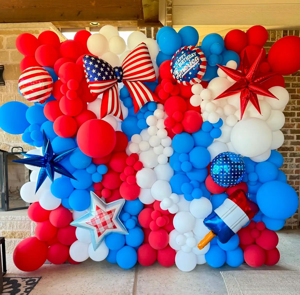 Full red, white, and blue balloon wall with an American-flag bow, striped foils, red and blue starbursts, a gingham star, and a Happy 250th Birthday America foil